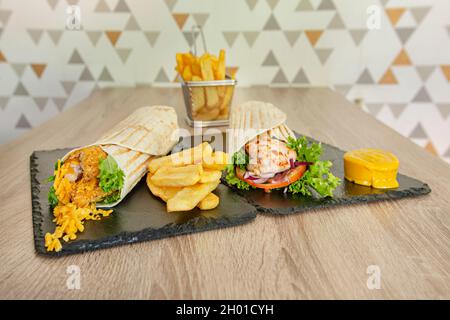 Gemischte Packung gefüllt mit gebratenem Huhn im Teig mit Gemüse und Senfsoße, gebratenem Fisch im Teig mit Cheddar-Käse und Pommes frites auf Woo Stockfoto