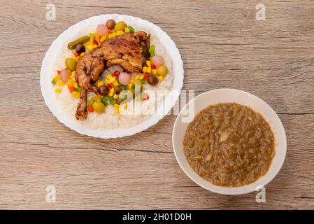 Typisches senegalesisches Rezept für yassa mit mariniertem, würzigem Huhn, weißem Reis und verschiedenen Gurken auf einem Holztisch Stockfoto