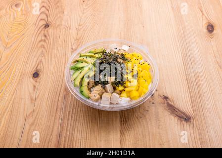 Vegane Poke-Schüssel im Take-away-Behälter mit Tofu, Mango, weißem Reis, reifer Avocado und geriebenem Nori-Seetang Stockfoto