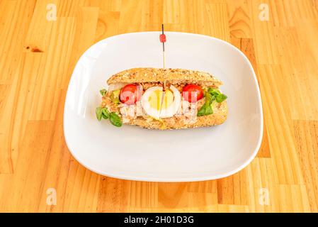 Sandwich mit Thunfischkonserven mit Tomate aus roter Kirsche, gekochtem Ei und Gemüse mit Samenbrot auf weißem Teller Stockfoto