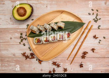 Sushi Uramaki california Roll mit rotem Thunfisch-Tartar, reifer Avocado und Sesamsamen mit Sternanis und hölzernen Essstäbchen mit Kürbiskernen und Banane Stockfoto