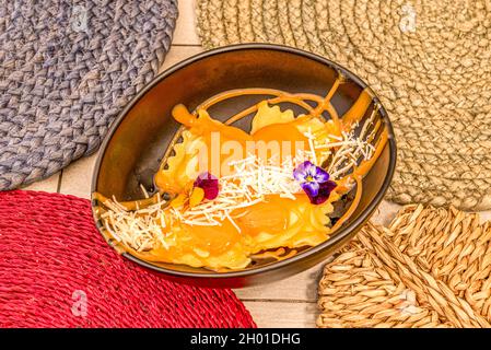 Frische Pasta Ravioli gefüllt mit Kürbis mit geriebenem Käse und essbaren Blumen auf schwarzer Schale Stockfoto