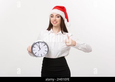Zeit-management Konzept - Junge Geschäftsfrau mit weihnachtsmütze Holding eine Uhr und zeigen thump auf weißem Hintergrund. Stockfoto