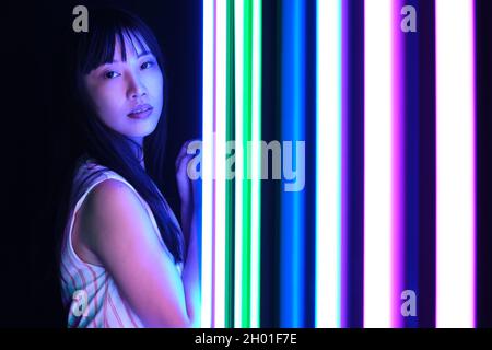Junge asiatische Frau posieren mit bunten hellen Neonlichtern im Studio. Stockfoto