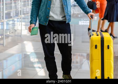 Mann, der am Flughafen Pass und Gepäck in seinem großen gelben Koffer in der Hand hält. Mann am Check-in-Schalter am Flughafen wartet vor dem Abflug Stockfoto