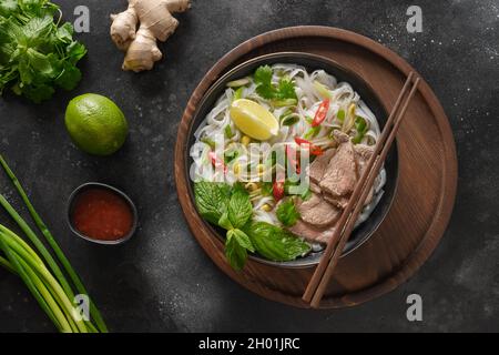Pho Bo traditionelle Suppe mit Rindfleisch, Reisnudeln, Ingwer, Limette, Chili in einer Schüssel auf schwarzem Hintergrund. Blick von oben. Vietnamesische und asiatische Küche Stockfoto
