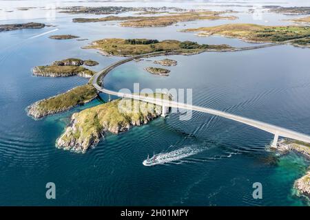 Luftaufnahme einer Brücke, die Inseln an der norwegischen Küste verbindet, Fischerboot, das unter der Brücke vorbeifährt, Norwegen Stockfoto