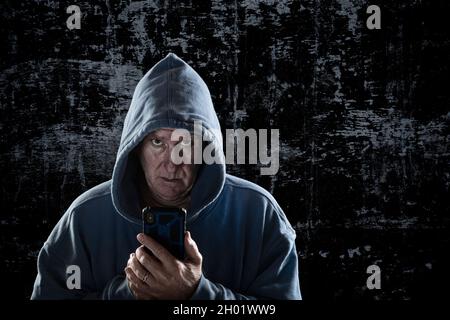 Ein böse aussehender Mann mit durchdringenden Augen und einem Hoodie steht einschüchternd gegen eine verbündete Wand, die sein nächstes Opfer verfolgt. Stockfoto