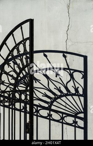 Detail von gusseisernen durchbrochenen Toren mit kontrastierendem Schattenmuster an der Vintage-Wand, herbstlicher sonniger Tag, architektonischer Hintergrund Stockfoto