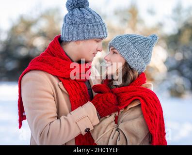 Nahaufnahme Foto von schönen romantischen jungen Paar Kuscheln in Winterwäldern, liebevoller Mann flüstert Worte der Liebe seine hübsche Freundin, umarmt, verschneite t Stockfoto
