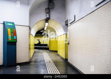 Leerer unterirdisch liedener Metro-Korridor mit Hilfseinrichtung für Defibrilatoren links und einsamer Mann, der unter dem Placa Molin wartet Stockfoto