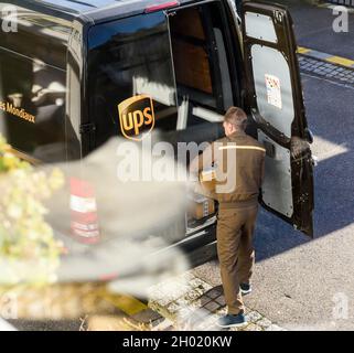 Luftaufnahme des UPS-Fahrers in Uniform neben seinem braunen Van, der das Paket mit dem neuesten E-Commerce auslädt Stockfoto