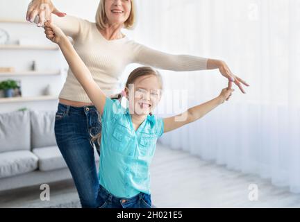 Überglücklich reife Frau mit Spaß genießen Zeit zusammen mit Enkelin zu Hause, glücklich ältere Dame und kleine niedliche Mädchen tanzen im Wohnzimmer, gran Stockfoto