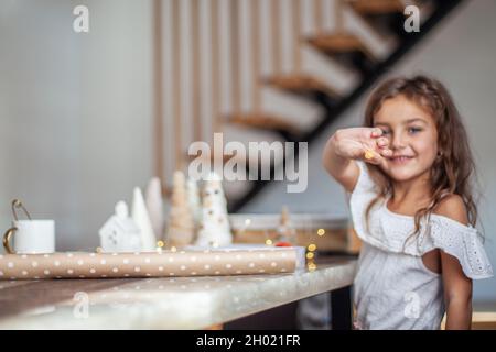 Nettes kleines Mädchen mit lockigen Haaren basteln und dekorieren Weihnachtsbaum Kegel mit Knöpfen. Stockfoto