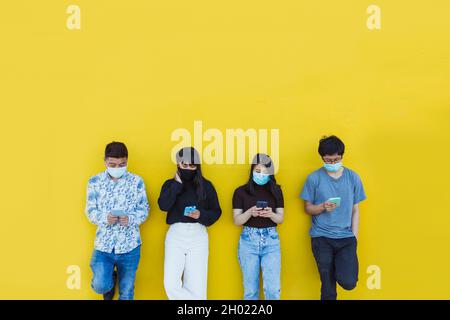 Asiatische Freunde in schützende Gesichtsmaske mit Smartphone im Freien Stockfoto