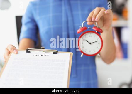 Geschäftsfrau hält roten Wecker und Vertrag auf Zwischenablage Stockfoto