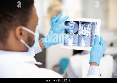 African American Male Dentist Doctor mit Digital Tablet, Überprüfung der Zähne des Patienten Röntgenbild während der Arbeit in der modernen Zahnklinik, Professional S Stockfoto