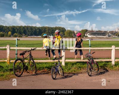 Caen, Normandie, Frankreich, Oktober 2021. Eine Mutter und Kinder sitzen am Zaun und beobachten Sport. Stehende Fahrräder neben ihnen. Eine Fahrradtour für die ganze Familie Stockfoto