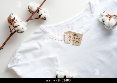 Weißes T-Shirt aus Bio-Baumwolle und Blumen aus Baumwolle auf der Tischansicht. Öko-Bekleidung, nachhaltiges Lifestyle-Konzept Stockfoto