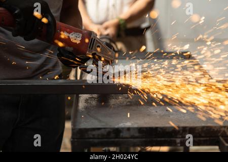 Nahaufnahme der Hände einer Person, die schwarze Schutzhandschuhe trägt, während sie ein Metallpolierwerkzeug verwendet, Funken von den Maquilas, manuelle Maschinenarbeiten Stockfoto