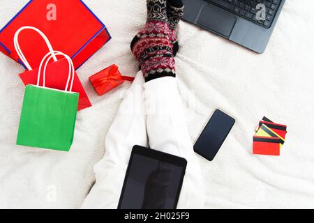 Weihnachts-Online-Shopping-Konzept mit Internet, Geschenktüten und Karten auf dem Bett Stockfoto