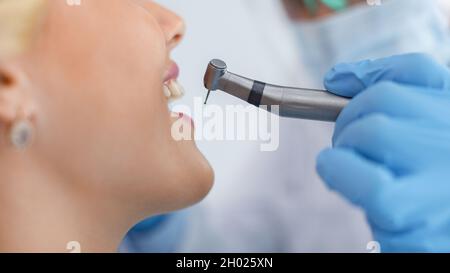 Aus jungen lächelnden blonden Frauen und Zahnarzthände in blauen Räuberhandschuhen mit Drillmaschine, Seitenansicht, Panorama. Nicht erkennbare weibliche Patientin vi Stockfoto