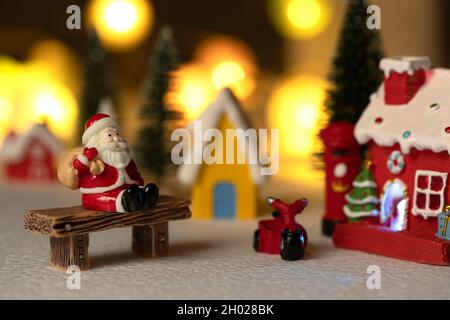 Der Weihnachtsmann sitzt zurück und entspannt sich vor dem Briefkasten mit einer rot-gelben Hütte mit Schnee auf dem Dach. Stockfoto