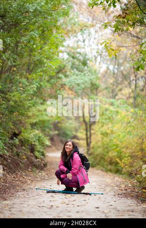 Hiker Mädchen hocken auf einem Weg in den Bergen. Rucksacktourist mit rosa Jacke in einem Wald. Gesunder Fitness-Lebensstil im Freien. Stockfoto