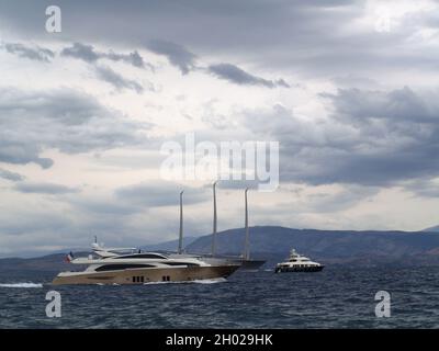 Große Motoryachten beschleunigen die größte Yacht der Welt "Sailing Yacht A", die vor der Küste in der Garitsa Bay, Korfu, Griechenland, verankert ist, mit kleinen Booten im Vordergrund Stockfoto