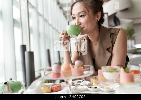 Reife asiatische Frau, die im Café in der Hotellobby am Tisch sitzt und Dessert isst und Tee trinkt Stockfoto