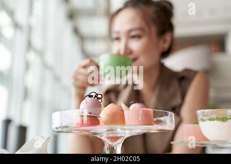 Reife asiatische Frau, die im Café in der Hotellobby am Tisch sitzt und Dessert isst und Tee trinkt Stockfoto