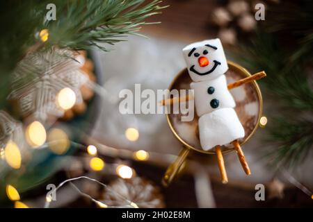 Ein Marshmallow Schneemann mit Glasur dekoriert. Goldbecher mit Kakao- und Weihnachtsdekor. Lebkuchen in Form von Schneeflocken. Stockfoto