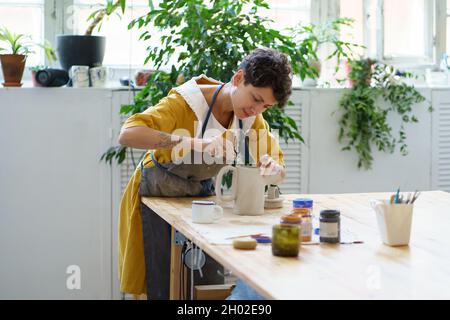 Junge weibliche Keramiker schmücken Töpfer Krug nach dem Brennen. Handwerkliche Keramik in Keramik-Werkstatt Stockfoto