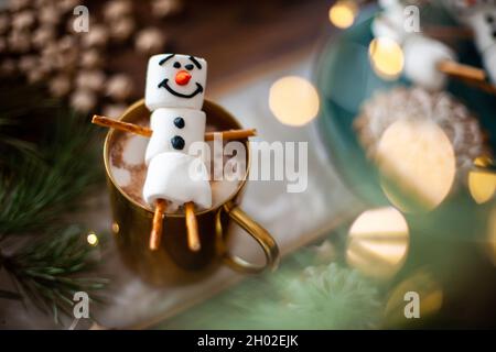 Ein Marshmallow Schneemann mit Glasur dekoriert. Goldbecher mit Kakao- und Weihnachtsdekor. Lebkuchen in Form von Schneeflocken. Stockfoto