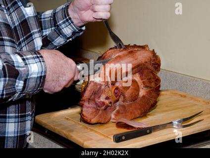 Die Hände des älteren Vaters schnitzen einen Schinken zum Abendessen Stockfoto