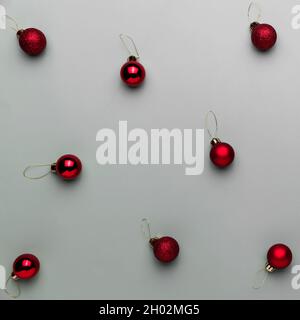 Muster auf grauem Hintergrund mit kleinen roten Weihnachtskugeln oder Kugelspielzeug für Tannenbaum. Konzept für festliche, minimalistische Grußkarte oder Einladung Stockfoto