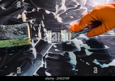 Orangefarbener Handschuh, Metallschaber und Schwamm. Reinigen des Kochfelds. Selektiver Fokus. Das Konzept der Hausreinigung eines Elektroofens Stockfoto