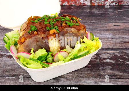 Gebackene, mit Chilischef gefüllte Jackenkartoffel mit frischem Salat in einer Take-Away-Box Stockfoto