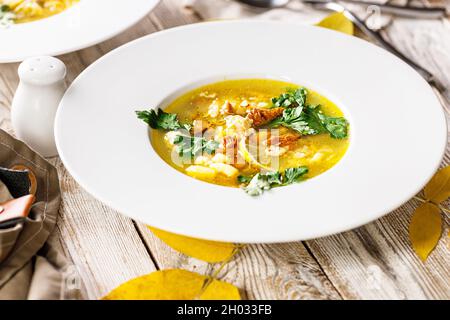 Köstliche Herbstsuppe mit Pfifferlingen und frischen Kräutern. Saisonales Gericht mit essbaren Pilzen. Weißer Teller und Besteck auf rustikalem Hintergrund. Essen sti Stockfoto