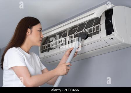 Junge Frau, die die Klimaanlage zu Hause mit einem Staubsauger reinigt Stockfoto