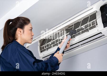 Eine Technikerin, die die Klimaanlage mit einem Staubsauger reinigt Stockfoto