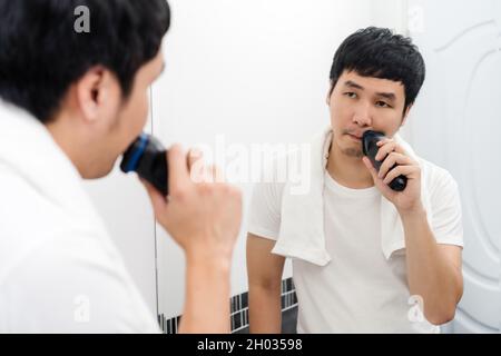 Mann, der sein Gesicht mit einer elektrischen Rasur im Badezimmerspiegel rasiert Stockfoto