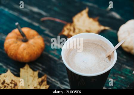 Nahaufnahme von Kaffee in Pappbecher mit Kürbissen und Ahornblättern im Hintergrund. Heißes Getränk. Herbstkomposition. Stockfoto