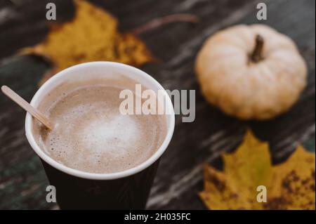 Nahaufnahme von Kaffee in Pappbecher mit Kürbis und Ahornblättern im Hintergrund. Heißes Getränk. Herbstkomposition. Stockfoto