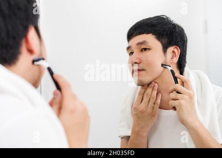 Mann mit Rasierer, um sein Gesicht ohne Schaum zu rasieren, Trockenrasur im Badezimmerspiegel Stockfoto