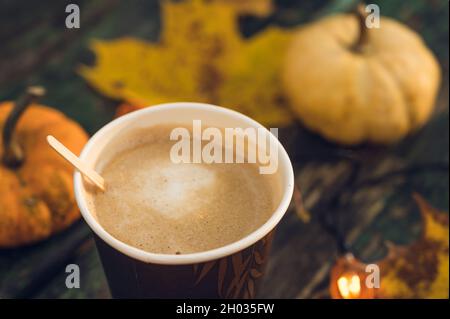 Nahaufnahme von Kaffee in Pappbecher mit Kürbissen und Ahornblättern im Hintergrund. Heißes Getränk. Herbstkomposition. Stockfoto