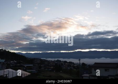 Iida, Nagano, Japan, 2021-11-10, von der Sonne beleuchtete Wolken während des Sonnenaufgangs am frühen Morgen über der Stadt Iida in Nagano, Japan. Stockfoto