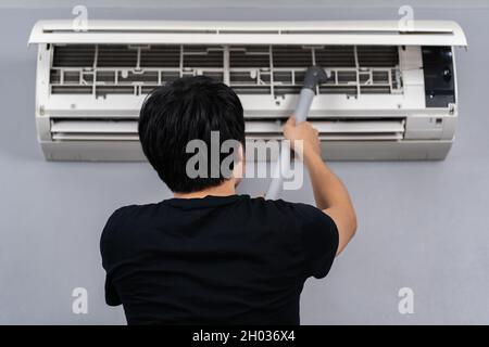 Junger Mann, der die Klimaanlage zu Hause mit einem Staubsauger reinigte Stockfoto