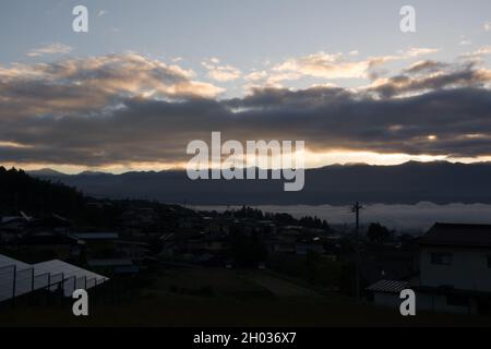 Iida, Nagano, Japan, 2021-11-10, von der Sonne beleuchtete Wolken während des Sonnenaufgangs am frühen Morgen über der Stadt Iida in Nagano, Japan. Stockfoto
