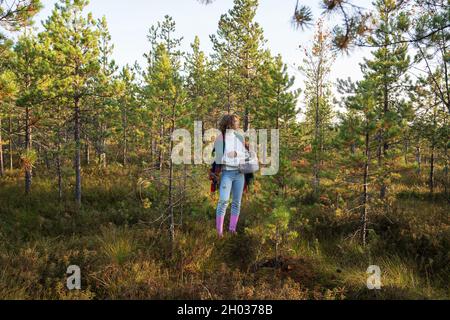 Casual Mädchen in Gummistiefeln genießen warmen sonnigen Tag Spaziergang Pick Cranberries im Herbst Wald. Herbstsaison Stockfoto